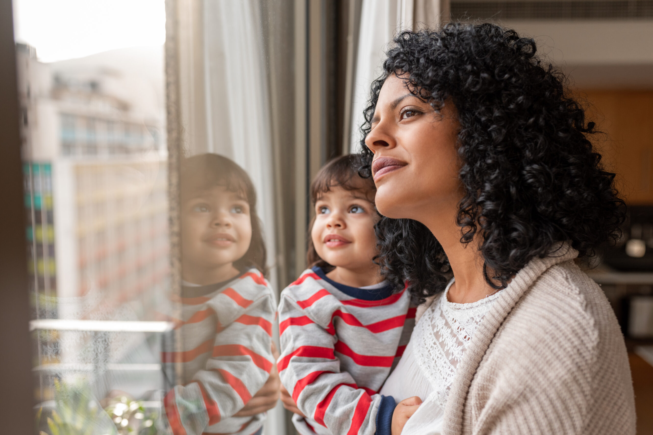 Woman with dark hair looking out the window holding a child, both smiling.